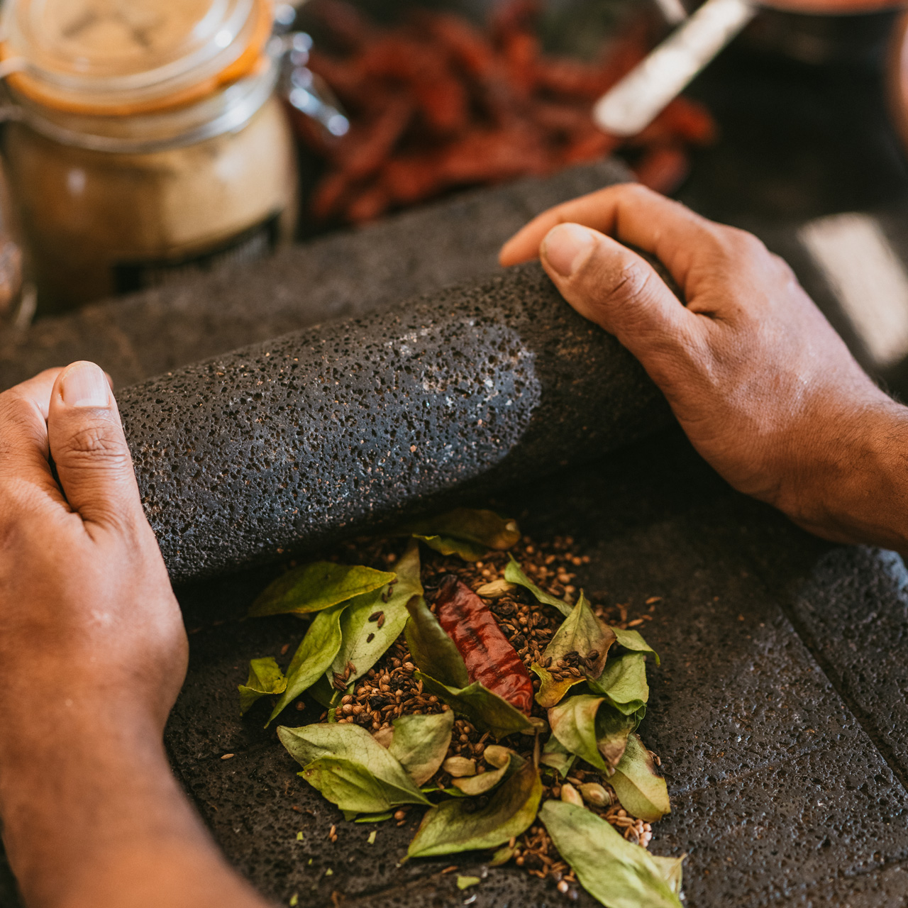 Hands grinding fresh herbs and spices with a traditional stone mortar and pestle, celebrating authentic local flavours and time-honoured culinary traditions.