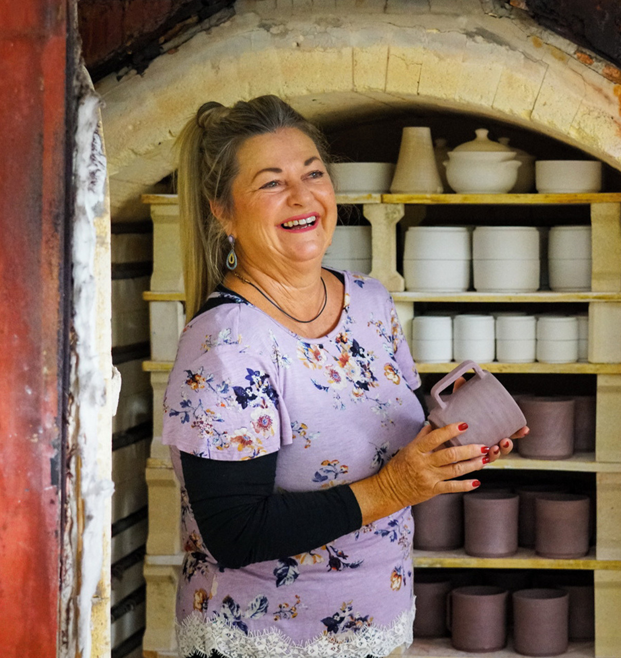 A local ceramic artist smiles beside a traditional kiln, showcasing handcrafted pottery inspired by local craftsmanship and creative expression.