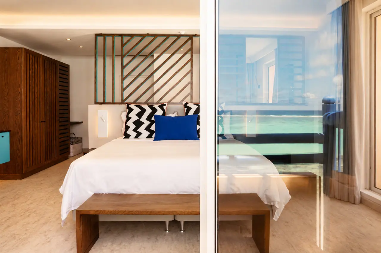 King-size bed with bold patterned cushions and contemporary wooden detailing in a bright hotel bedroom.