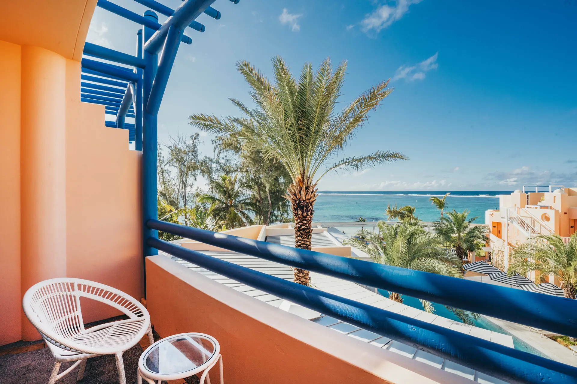 Private balcony overlooking the hotel, palm trees, and the turquoise ocean.
