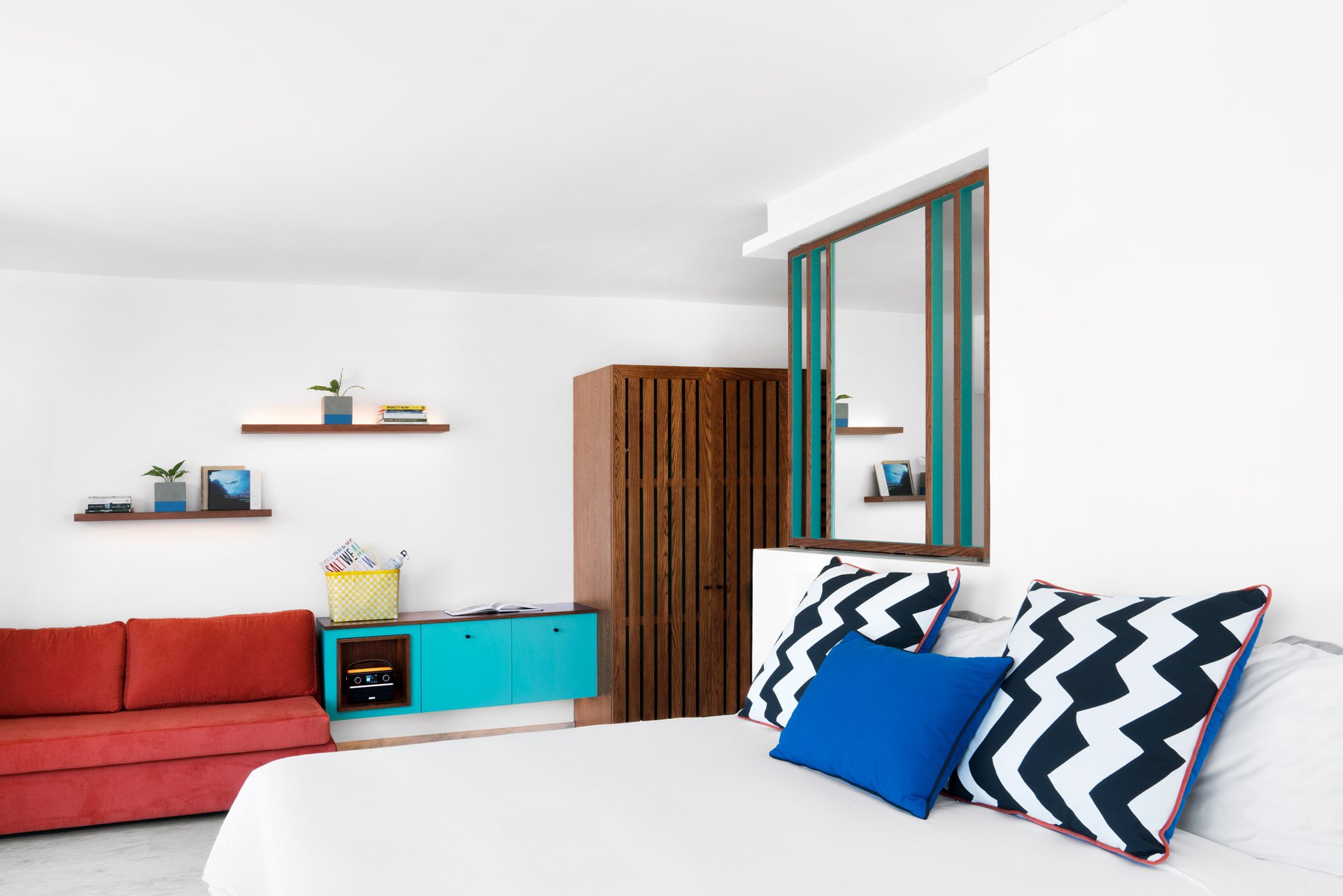 Modern hotel bedroom with a lounge area, colourful design accents, and contemporary furnishings.