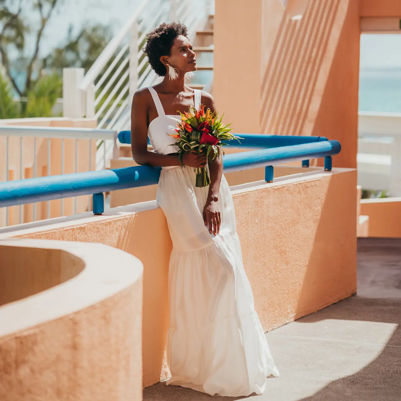 Mariée tenant un bouquet tropical sur une terrasse ensoleillée.