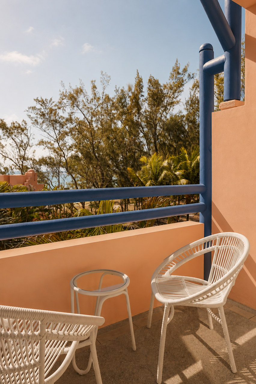 Private hotel room balcony with outdoor seating overlooking tropical gardens and glimpses of the ocean.