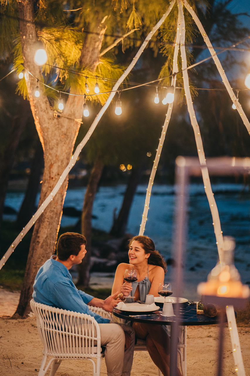 Couple dînant au bord de la plage sous des guirlandes lumineuses.