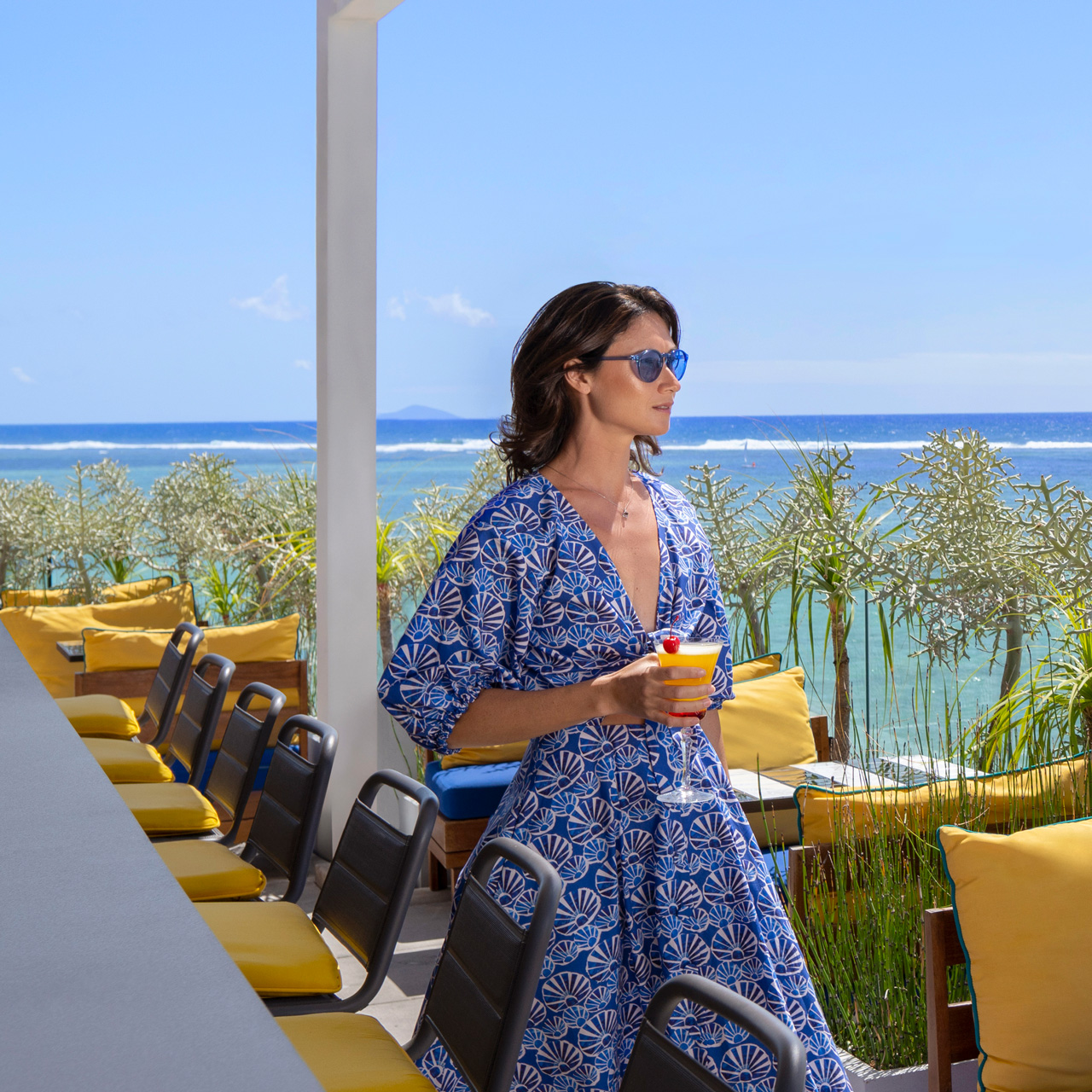 Cliente savourant un cocktail sur le rooftop avec vue sur l'océan.