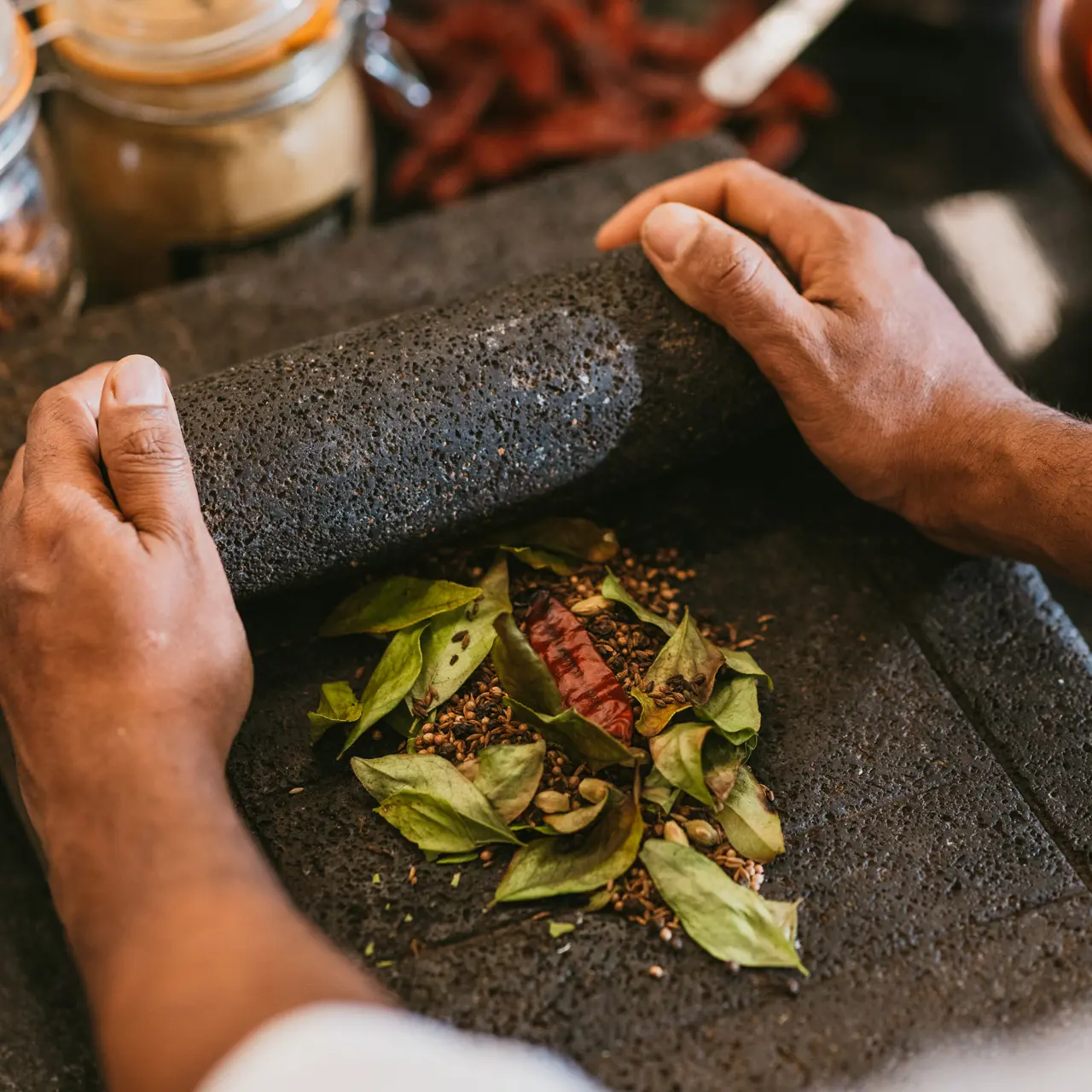 Hands grinding fresh herbs and spices with a traditional stone mortar.