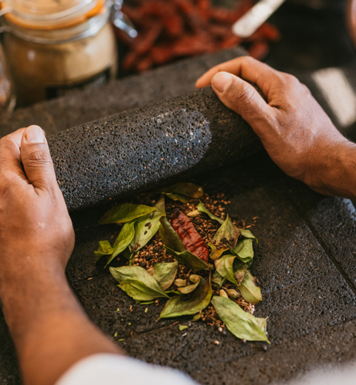 Hands grinding fresh herbs and spices with a traditional stone mortar.