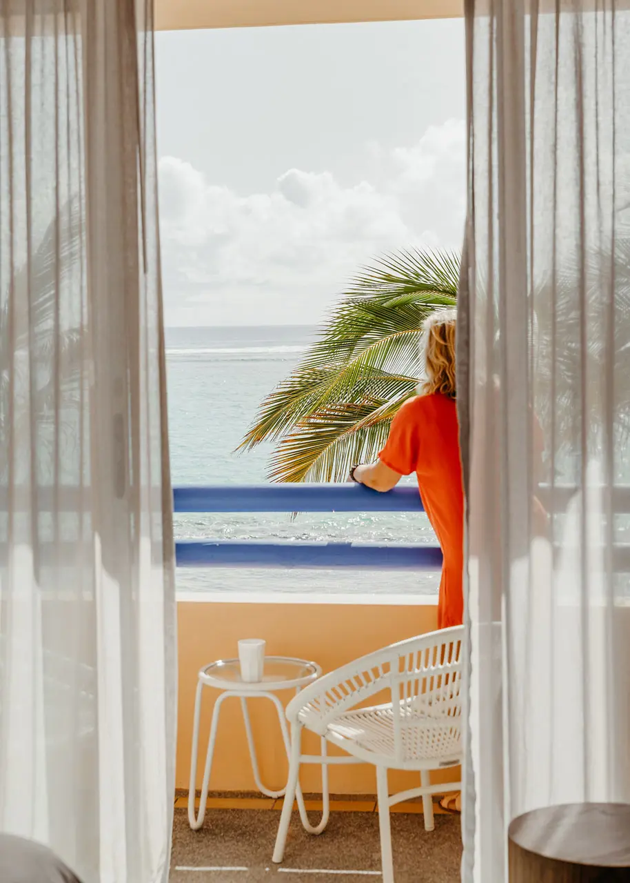 Guest enjoying ocean views from a private balcony framed by tropical palms.
