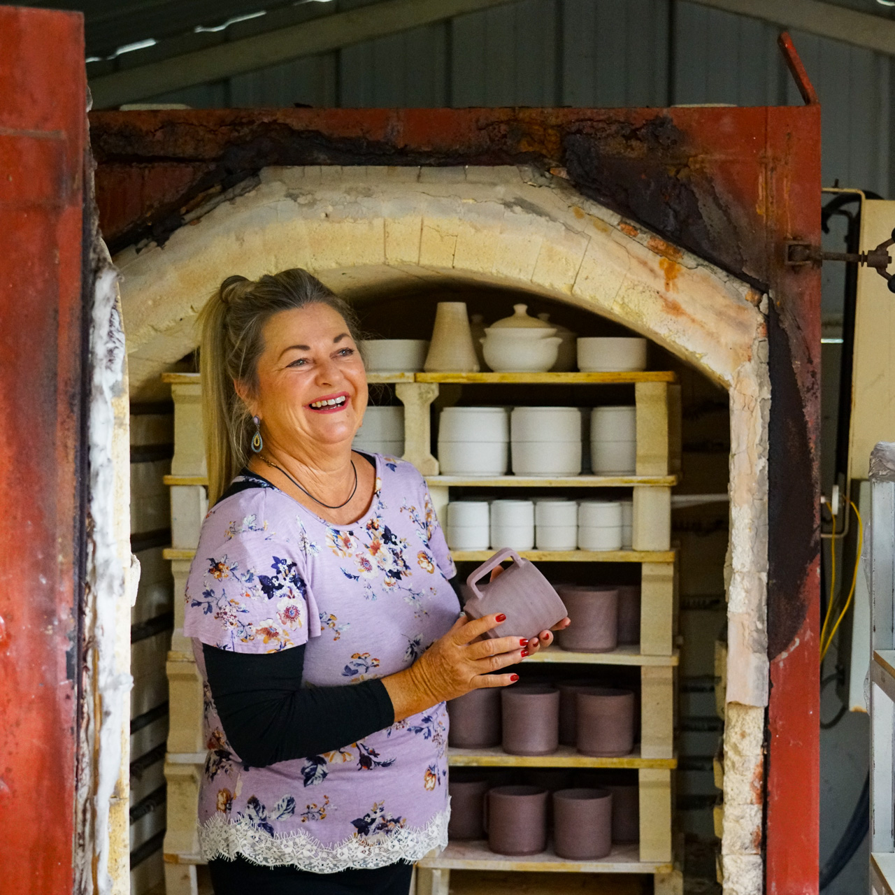 Ceramic artist Janine beside her kiln with handmade pottery.