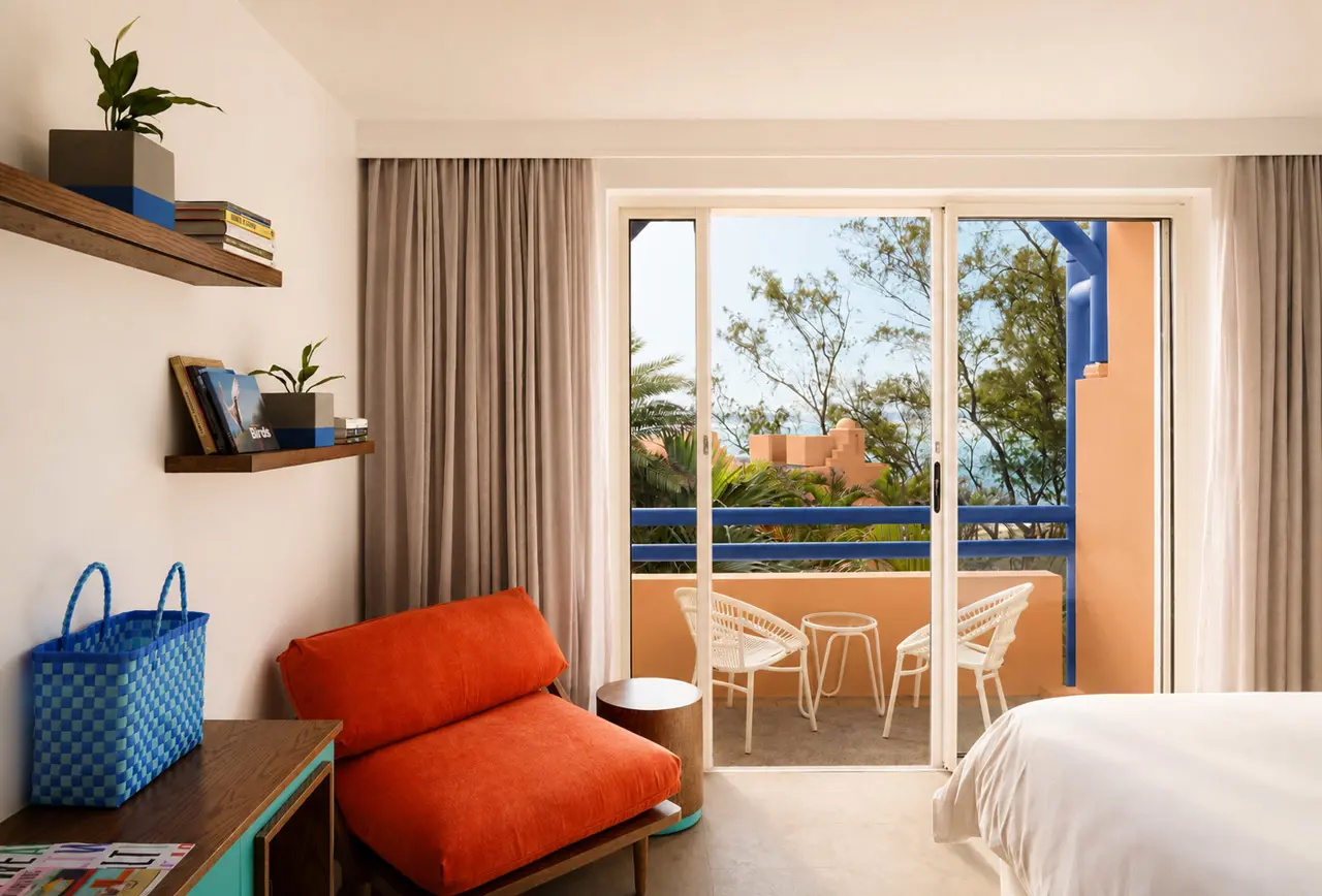 Contemporary hotel room with a private balcony, colourful lounge chair, and views of tropical gardens.