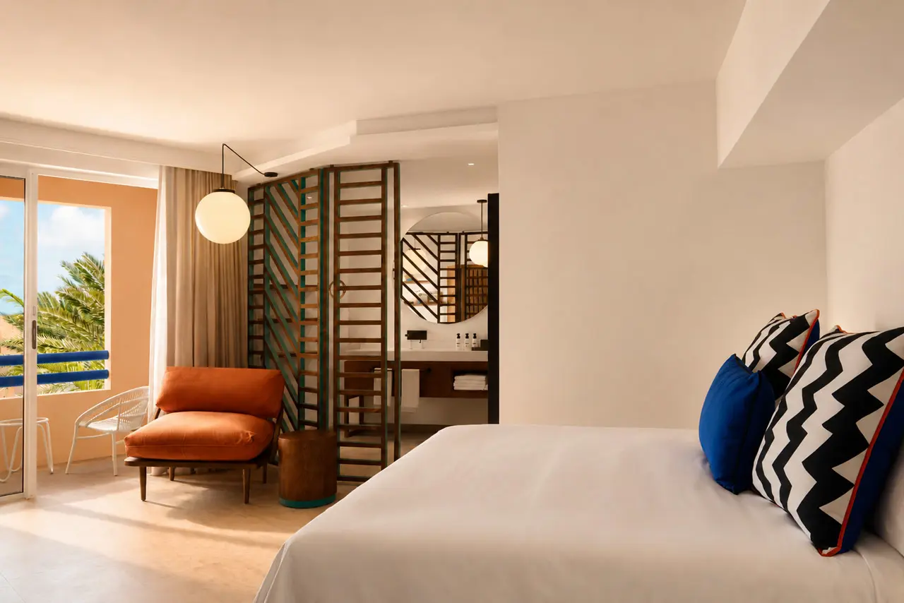 Contemporary hotel room with a private balcony, ocean views, and warm natural light.