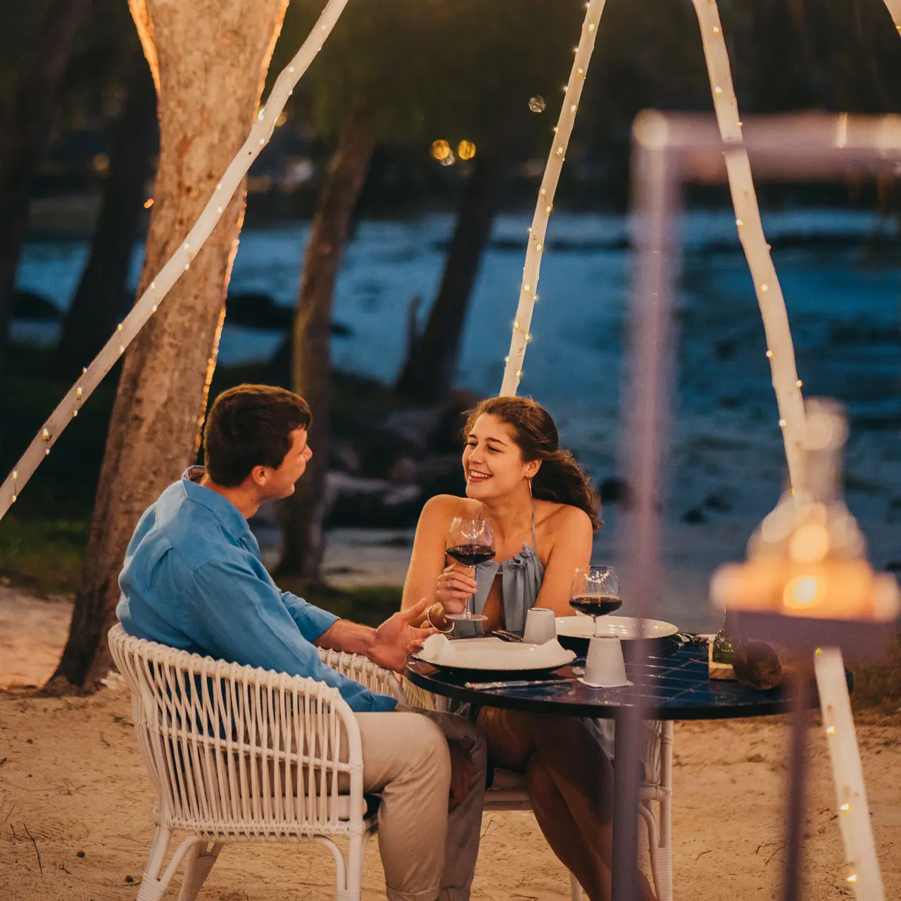 Couple enjoying a romantic beachfront dinner with wine at sunset.