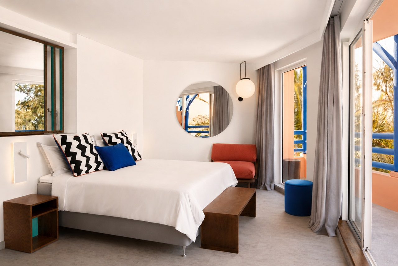 Modern hotel bedroom with a private balcony, colourful design accents, and views of tropical greenery.