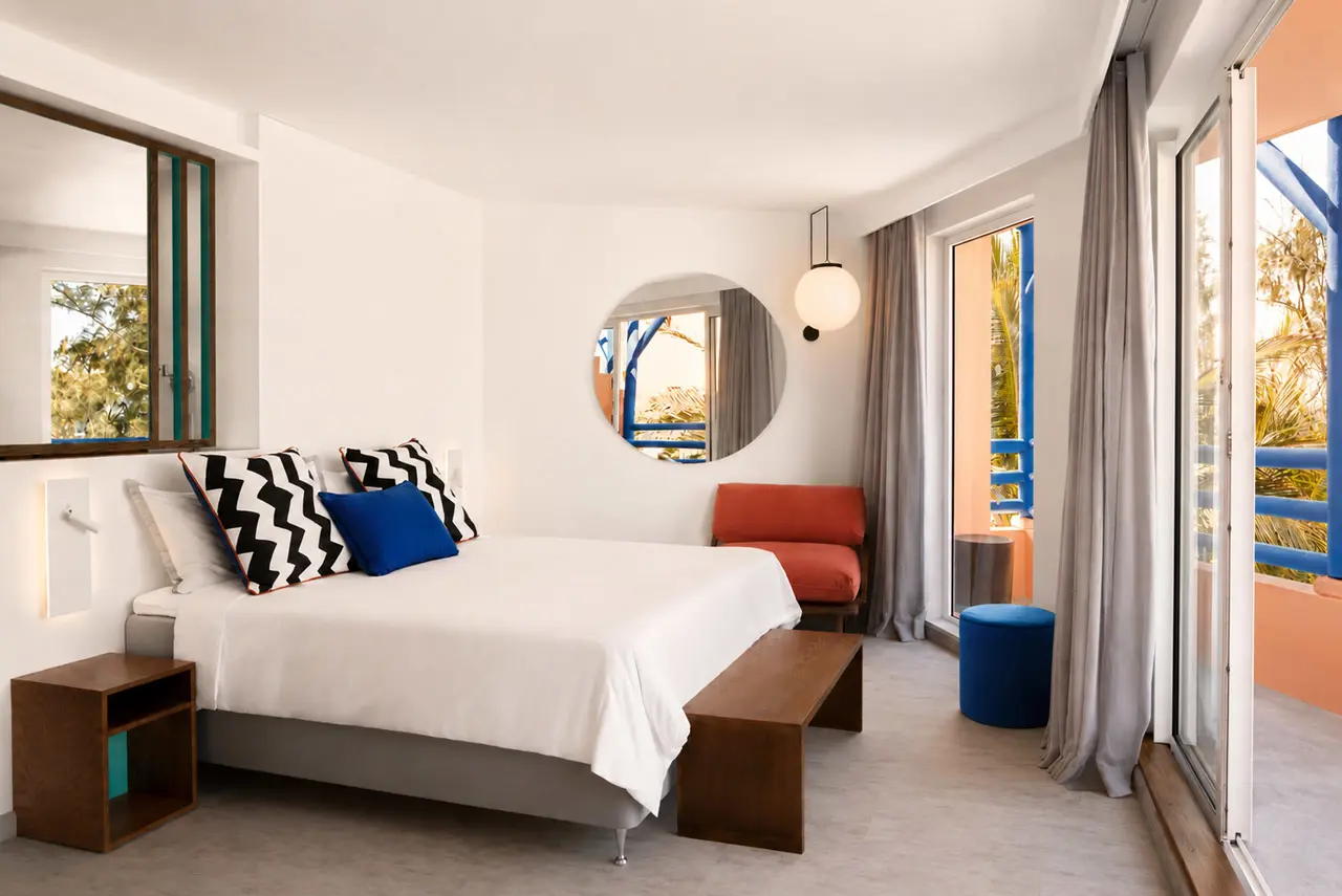Modern hotel bedroom with a private balcony, colourful design accents, and views of tropical greenery.