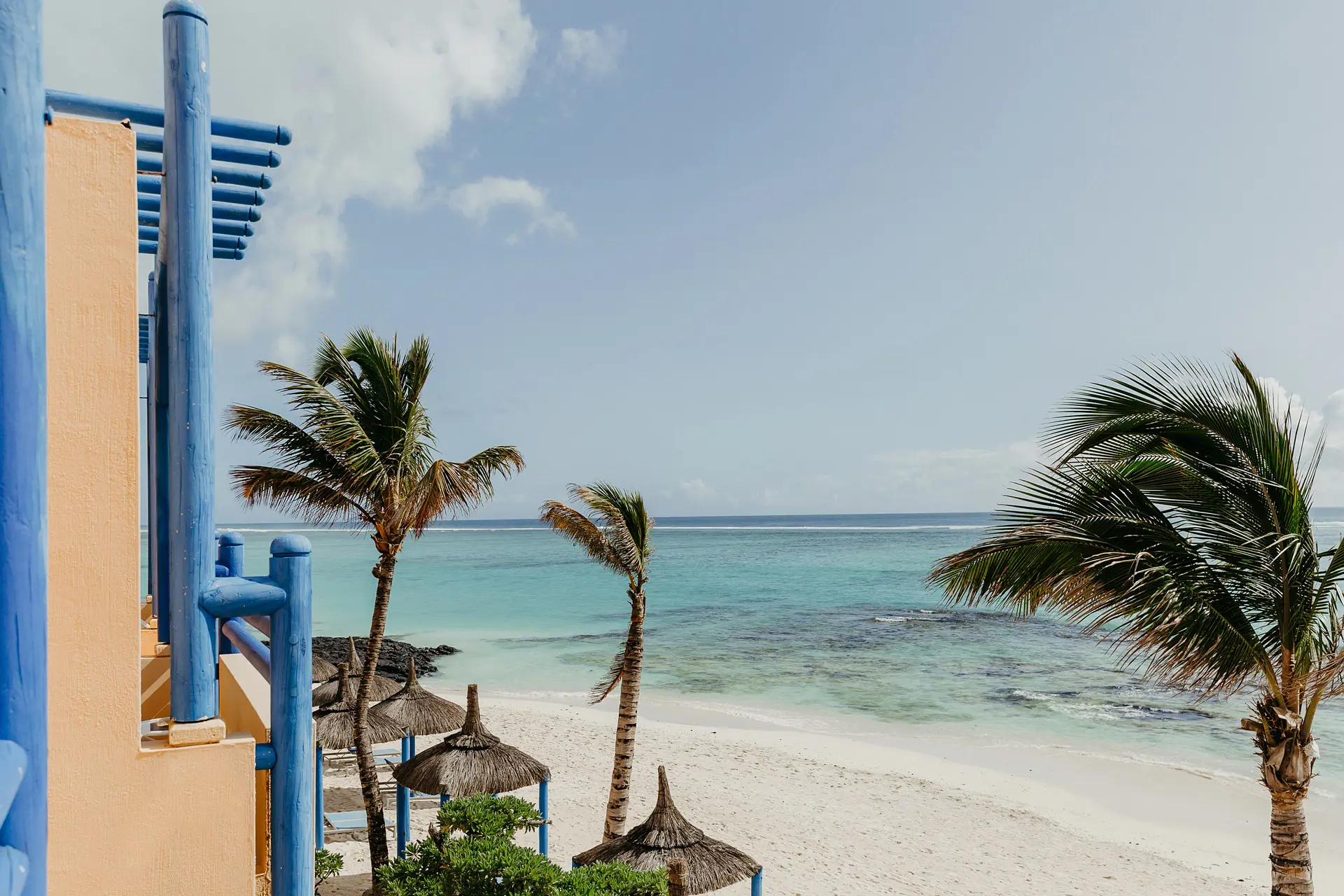 Beachfront view with turquoise lagoon, palm trees, and white sandy shores.