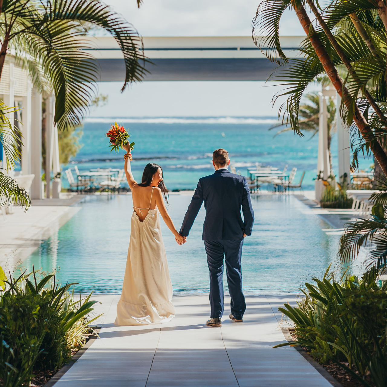 Newlyweds walking hand in hand towards the ocean.
